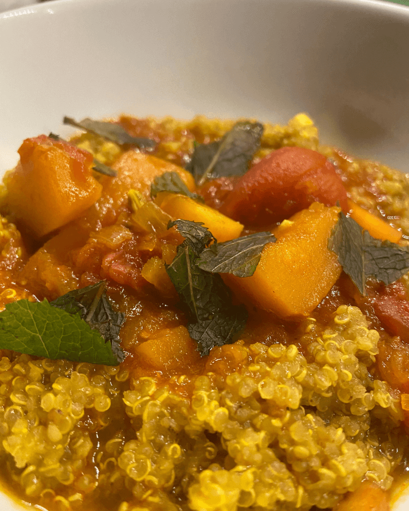 bowl of vegan spiced quinoa curry with butternut squash, carrots, tomatoes, and mint leaves 