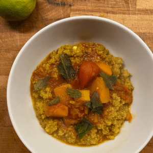 bowl of vegan spiced quinoa curry with butternut squash, carrot, and mint leaves on top