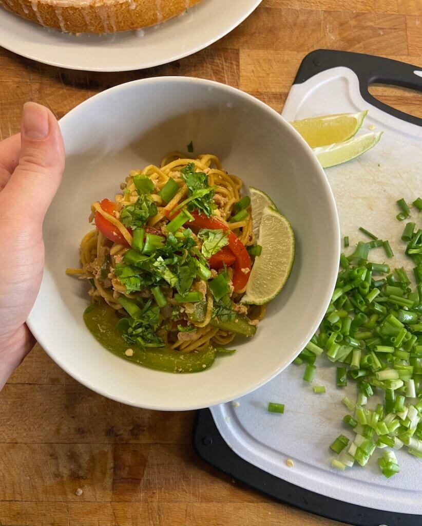 bowl of ground turkey stir fry noodles with bell peppers, green onions, corainder and lime wedges 