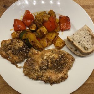 za'atar breaded chicken with spiced veggies on the side and two slices of olive bread