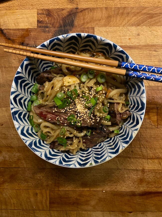 bowl of ram-don or jjapaguri noodles with decorated chopsticks, topped with green onions and sesame seeds