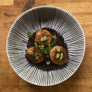 A bowl of pork meatballs on a bed of black Thai rice, topped with spring onions